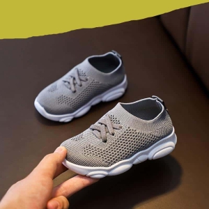 Une paire de baskets chausson grises antidérapantes tenue dans la main d'un adulte