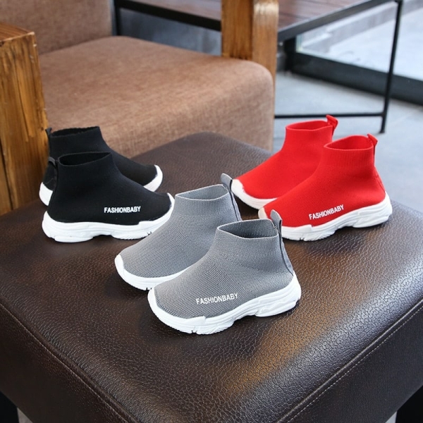 A pair of casual high-top trainers for girls in red, black and grey tones, shown on a chair in a home setting