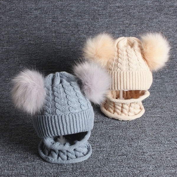 Both colour options of the pom-pom hat with integrated scarf laid side by side, showing the pink and grey versions in full detail.