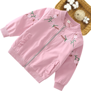 A pink girls bomber jacket with beautiful embroidered flowers and bow detail displayed next to a wicker basket, elegant and playful.