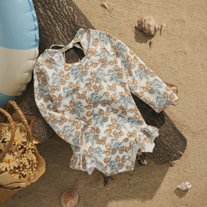 Girls long-sleeve patterned swimsuit laid on driftwood on a beach with decorative accessories