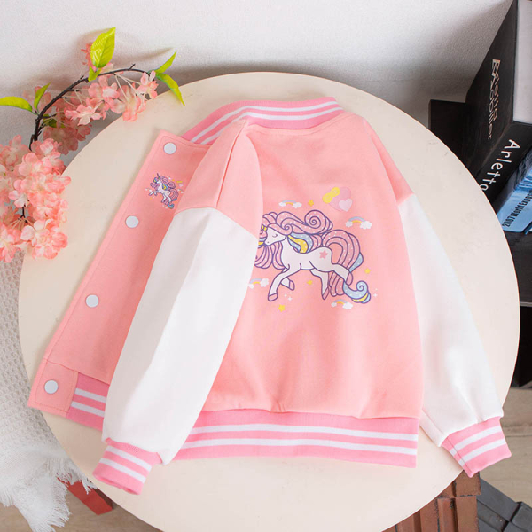 A pink and white unicorn print girls bomber jacket laid on a round table, fun and stylish for a magical everyday look.