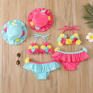 Two matching swimsuit and hat sets in pink and blue with fabric flower detail, laid on parquet flooring