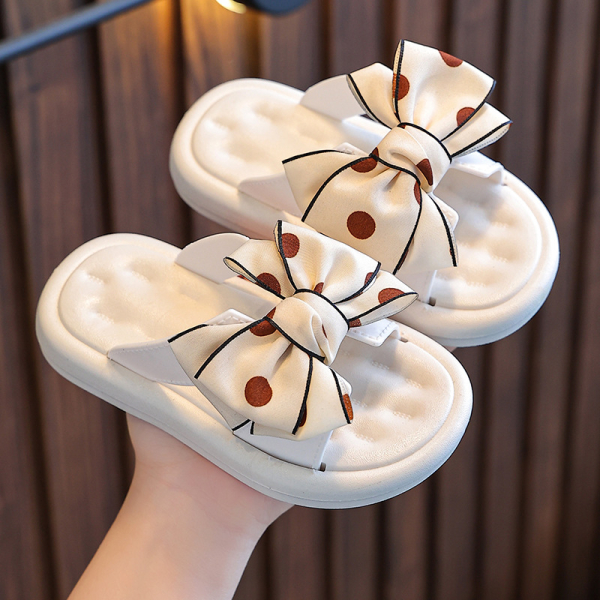 White girls sandals with a red polka dot bow, held in one hand, fun and summery