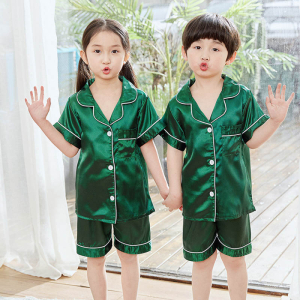 Girl and boy standing with one hand raised, both wearing a flowy green satin summer pyjama set