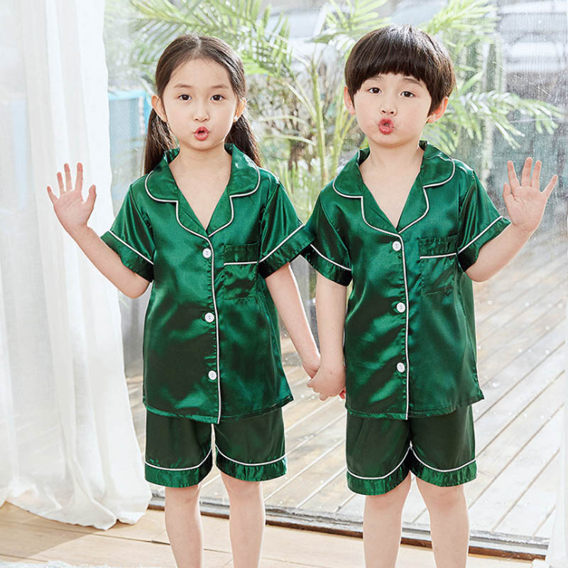 Girl and boy standing with one hand raised, both wearing a flowy green satin summer pyjama set